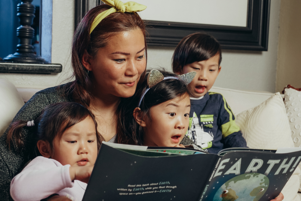 mom with three young children reading a children's book together