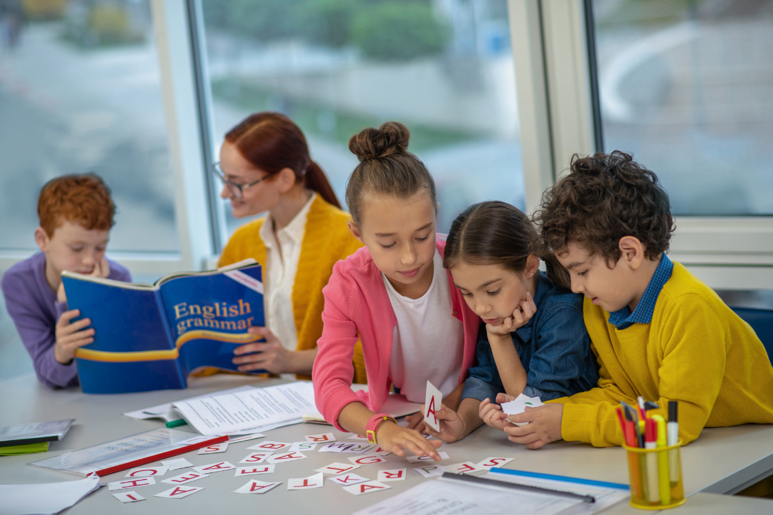 children sitting at a classroom table playing with English alphabet cards